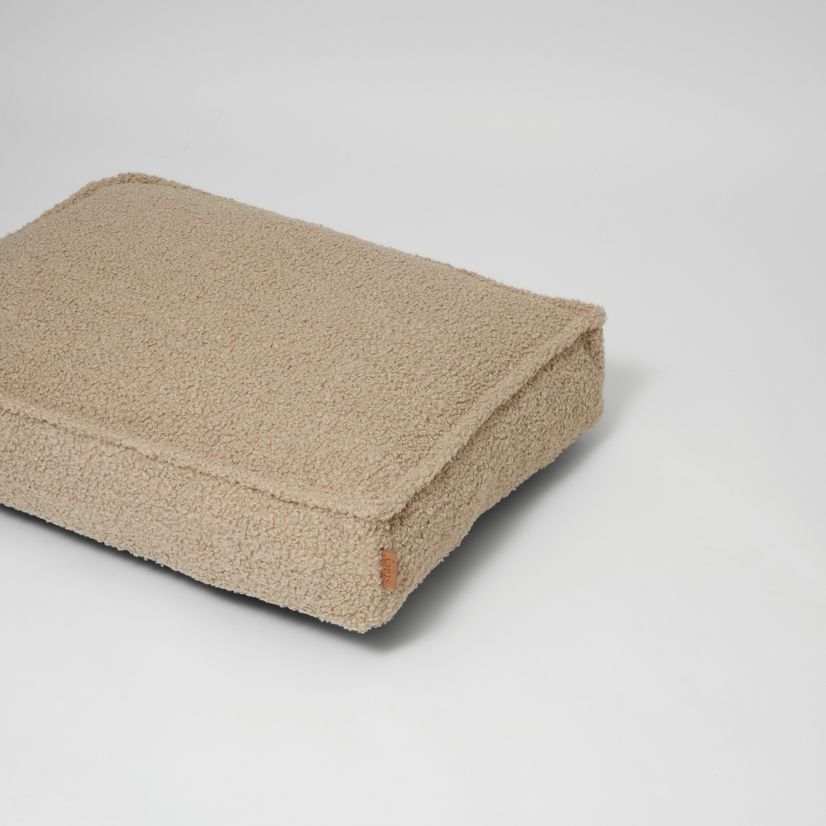 Het zandkleurige, gekrulde Bouclé-hondenmatras, vanuit een schuine hoek gezien