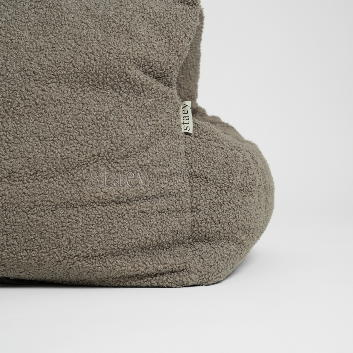 The moss green bouclé car seat seen from the side with its Staey label