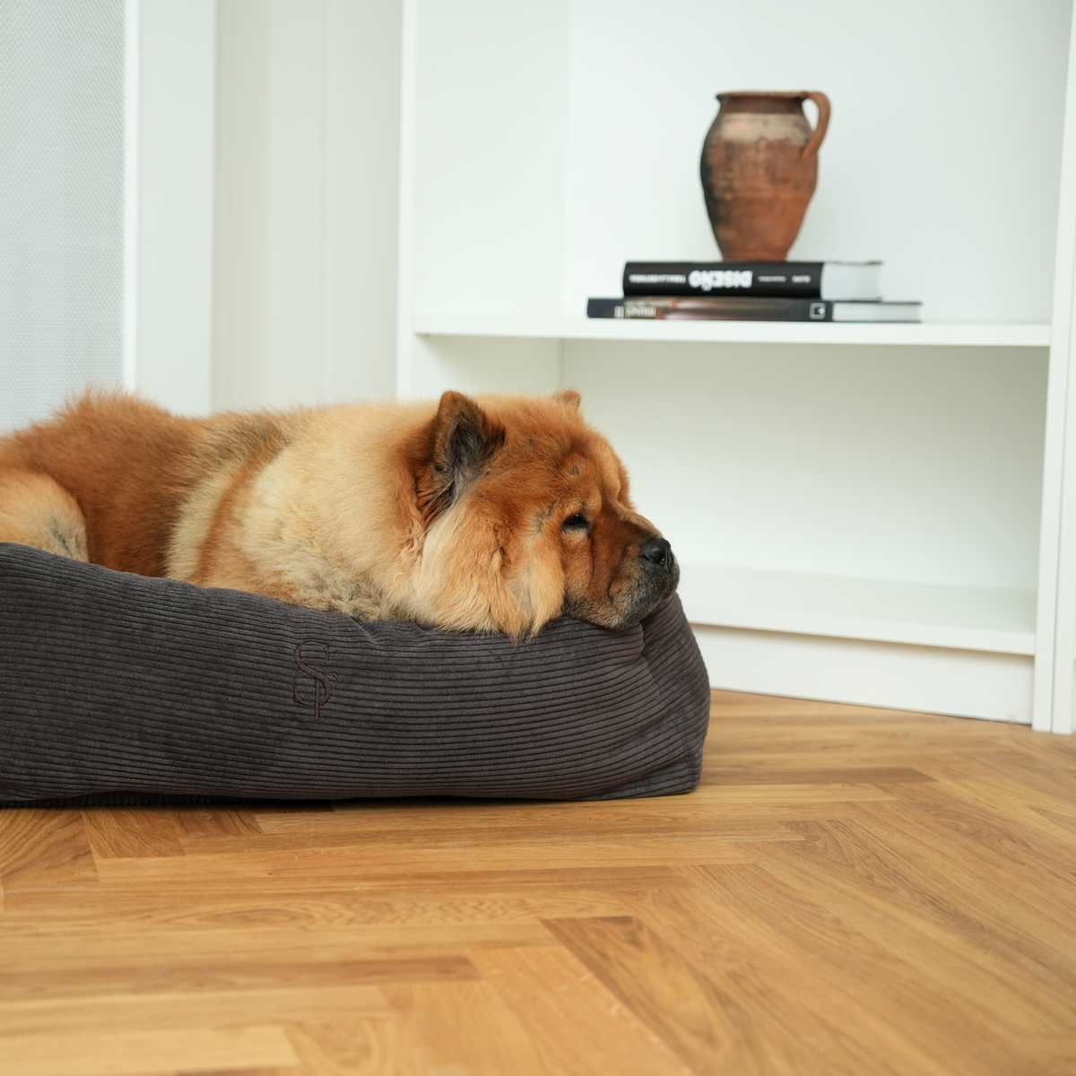 Een chowchow die in de hondenmand van antracietkleurig Corduroy op een parketvloer ligt