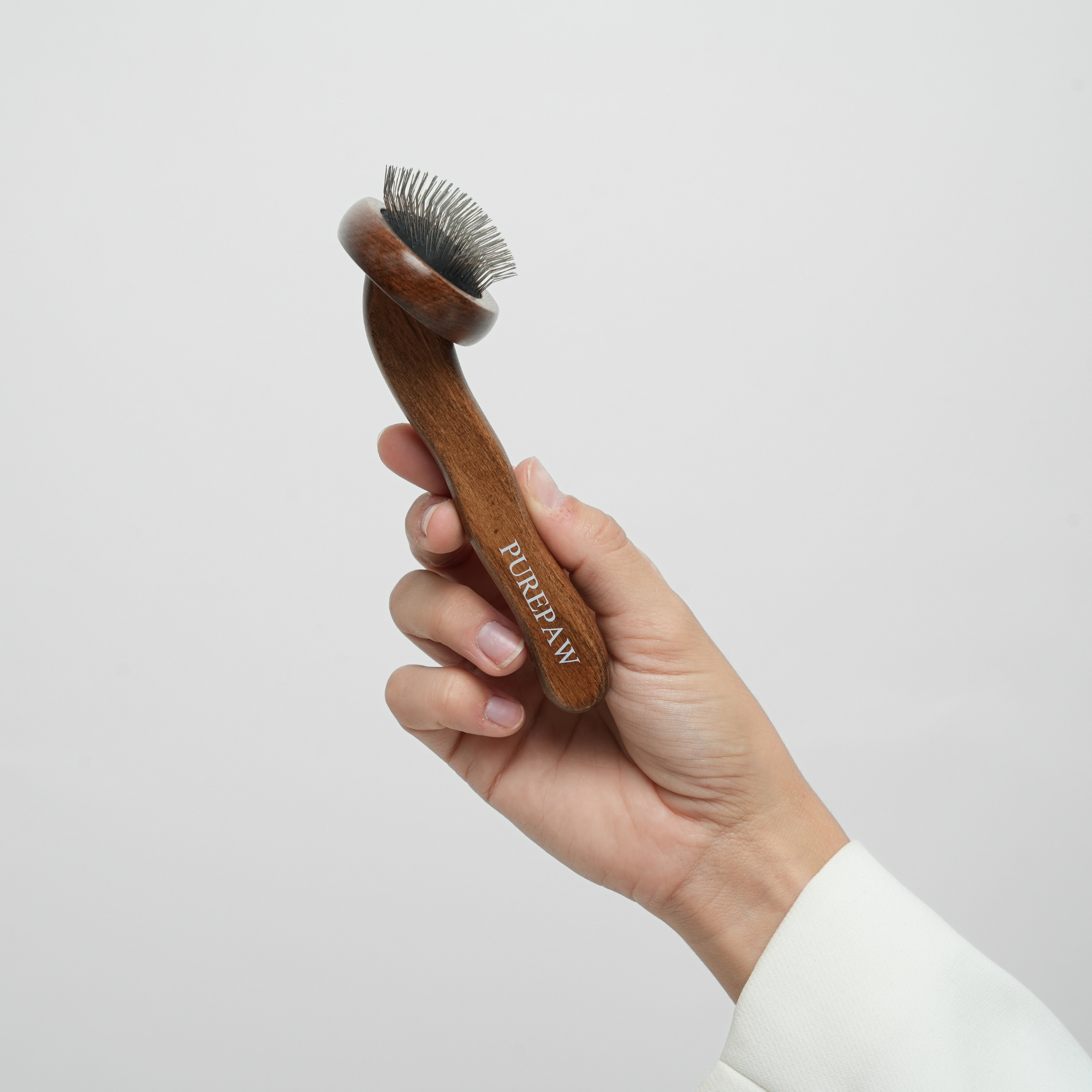 Hand met een houten borstel voor de verzorging van honden met het merk 'Purepaw' tegen een lichtgrijze achtergrond