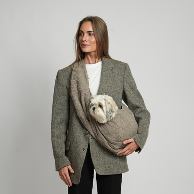 Woman carrying a small white dog in the Ava Teddy sling carrier